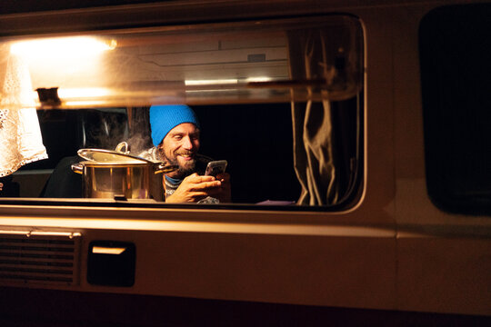 A young handsome guy playing with his phone while the food is cooking 