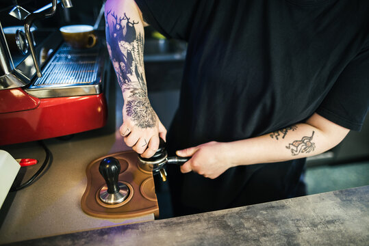 Crop female barista pressing coffee In portafilter
