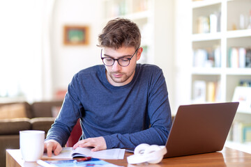 Junger Mann, freelancer oder Student, sitzt zu Hause am Schreibtisch mit einem Laptop und arbeitet...