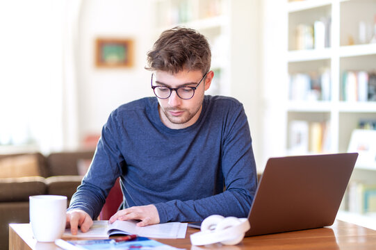 Junger Mann, freelancer oder Student, sitzt zu Hause am Schreibtisch mit einem Laptop und arbeitet konzentriert. Neben ihm steht eine Tee- oder Kaffeetasse. Auf dem Tisch liegen Kopfh&ouml;rer.