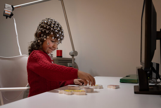 Kid in EEG cap playing with a puzzle in laboratory