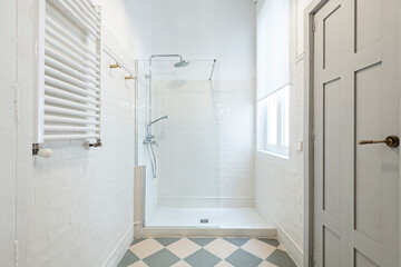 Bathroom with shower cabin with glass partition, white towel radiator, small white tiled tiling and gray wooden door