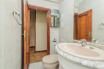 Toilet with pink bathroom fixtures, washbasin on white marble countertop and square mirror with...