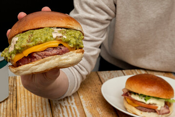 A person's hand holding a beef burger with cheddar cheese and lots of Mexican guacamole