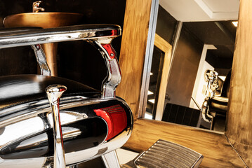 black leather armchairs with chrome in front of rectangular mirrors with gold frame in men's beauty salon