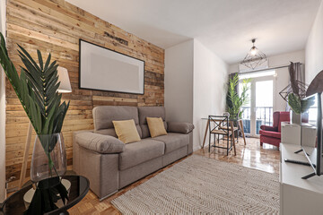 living room with wall covered in planks, palm leaf in a glass vase, gray two-seater sofa and natural fiber rug