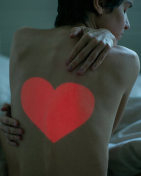 Woman in bed hugging herself with a heart on her back