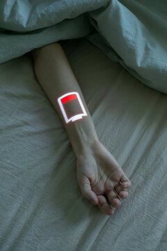 Rest in bed. Human hand with low battery symbol