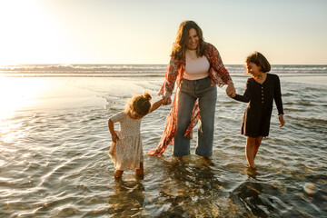 Obraz premium Mom and daughters wading in ocean surf