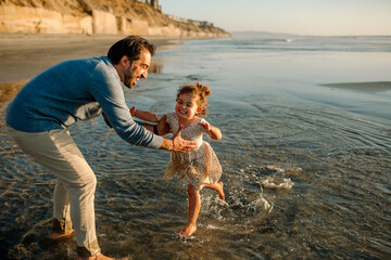 Fototapeta premium Father lifts joyful daughter from ocean