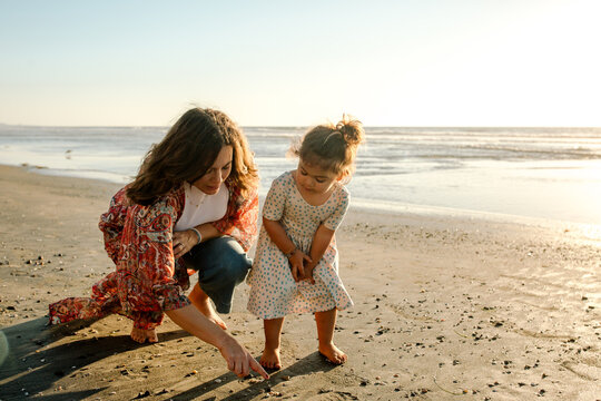 Mother and daughter looking at shells on beach