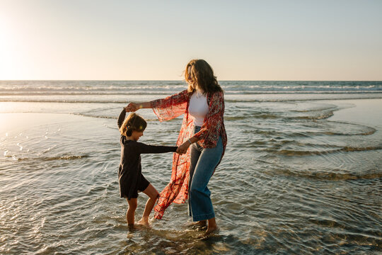 Mother and daughter dancing in surf at sunset