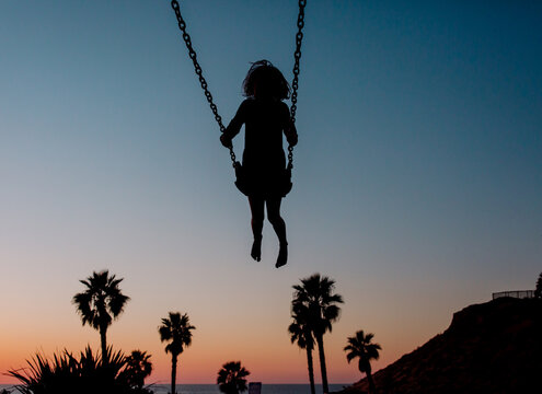 Silhouette of child on swing at sunset