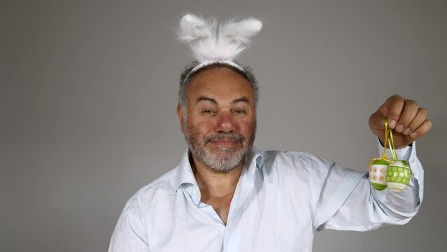 Easter Day. Funny bearded man wearing bunny ears holding easter eggs, smiling and talking. Handsome mature male with bunny ears. Easter bunny rabbit.