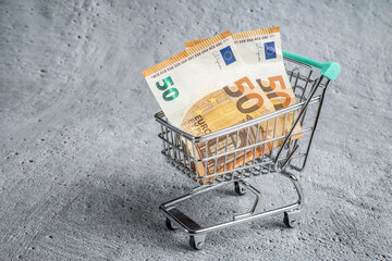 Shopping cart on cement background with money inside. Price increase due to inflation. Rising prices.