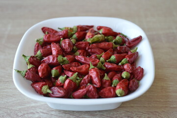 small extremely hot red peppers in a white bowl on a wooden table