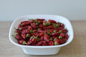 small extremely hot red peppers in a white bowl on a wooden table