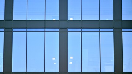 Fototapeta na wymiar Minimalist glass facade, steel framework holding the large transparent panels. Contemporary commercial architecture, vertical converging geometric lines. Blue sky reflection in the glass panels