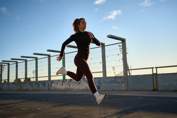 Woman jogger running along bridge in sunlight
