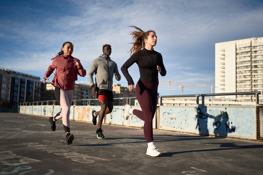 Diverse joggers running along bridge in sunlight