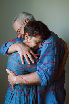 An elderly couple hugs and is tied with a red thread.