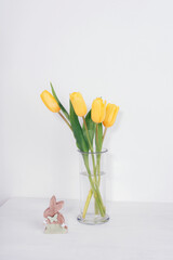 Yellow tulip flowers in glass vase and wooden toy rabbit. Easter concept. Front view