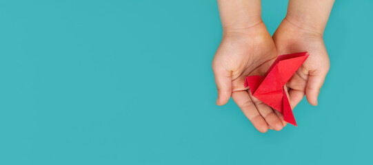 red paper origami pigeon in children's hands on a blue background