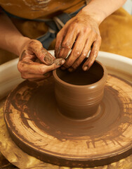 Fototapeta na wymiar A Potter works with red clay on a Potter's wheel in the workshop..Women's hands create a pot. Girl sculpts in clay pot closeup. Modeling clay close-up. Warm photo atmosphere. 