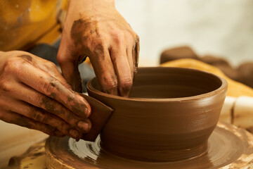 A Potter works with red clay on a Potter's wheel in the workshop..Women's hands create a pot. Girl sculpts in clay pot closeup. Modeling clay close-up. Warm photo atmosphere. 