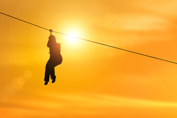 silhouette of side view of young woman riding on zip line on sunset background.
