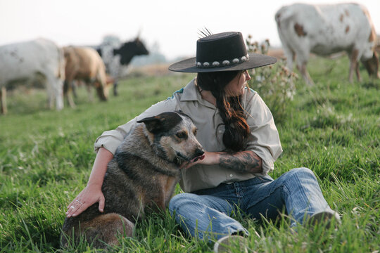 ranch woman sits with cow dog in pasture 