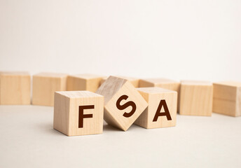 letters of the alphabet of FSA on wooden cubes, green plant on a white background. FSA - short for...