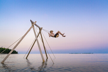 Fototapeta premium Boy on Lake Swing During Luxury Summer Vacation