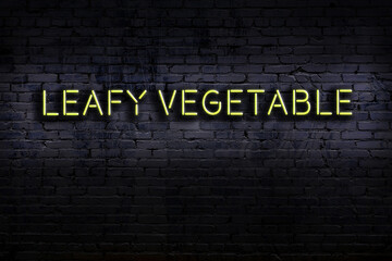 Neon sign. Word leafy vegetable against brick wall. Night view