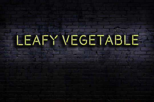 Neon sign. Word leafy vegetable against brick wall. Night view