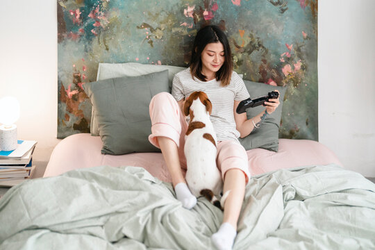 Woman with dog on bed with gamepad for smartphone