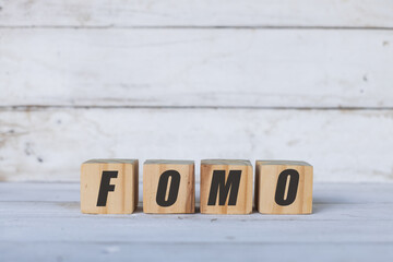 FOMO concept written on wooden cubes or blocks, on white wooden background.