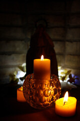 Trio de velas para pedir ayuda y milagros, con la Vírgen María de fondo con luces cálidas.