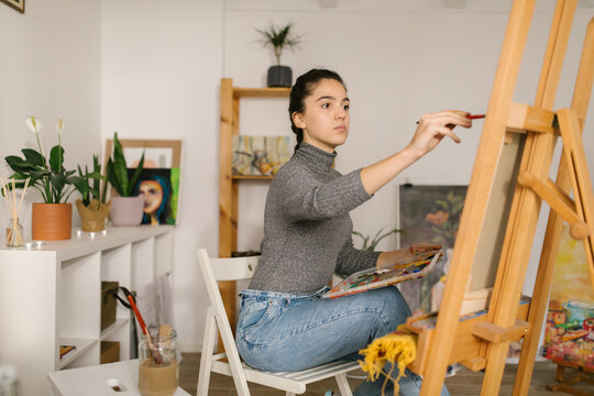 Young artist sitting and painting on canvas at home