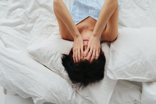 Sad woman with headache lying on bed