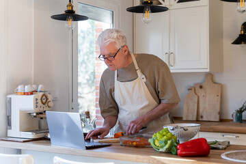 Senior man cooking with online tutorial on laptop