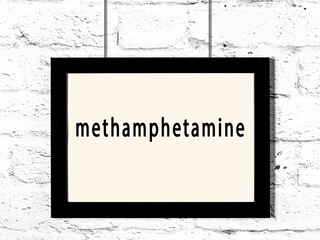 Black frame hanging on white brick wall with inscription methamphetamine