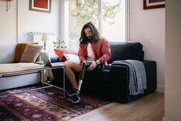 Person with a disability on sofa putting on leg prosthesis