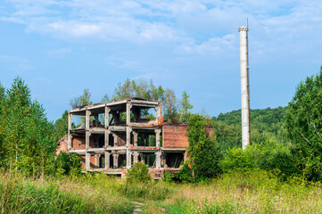 Old Abandoned brick industrial building with tall pipe surrounded by nature