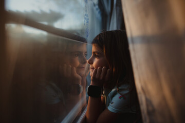 Young girls looks out window with sun setting outside 