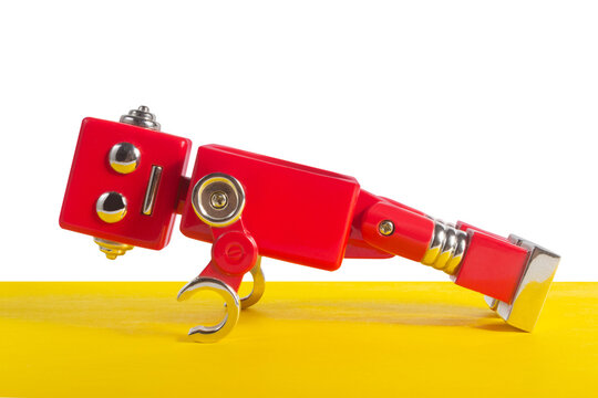 Photo of red colored metal robot toy doing push ups on yelllow floor background.