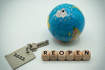 key bears label 2022, wooden dice on the side read 'reopen', Blurred globe on back. metaphor for...