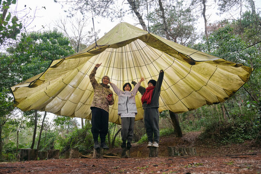 Asian family playing under large parachute outdoors

