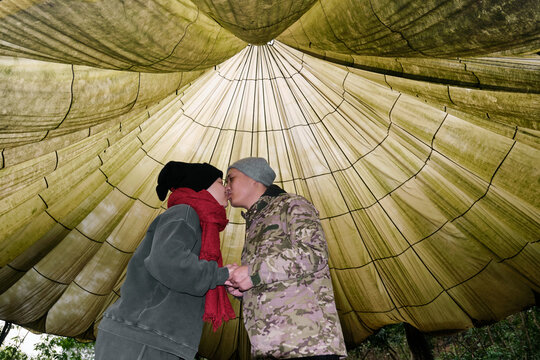 Asian couple kissing under large parachute outdoors

