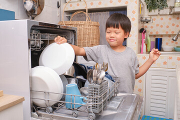 Cute Asian boy child having fun doing the dishes, washing dishes, loading the dishwasher in kitchen...